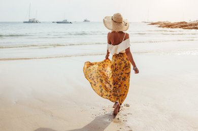 Donna sulla spiaggia con abiti leggeri e cappello