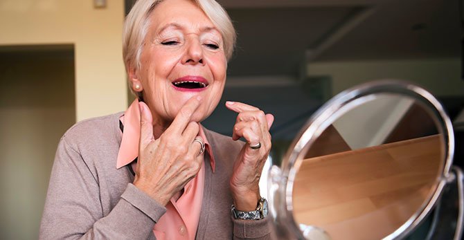 una donna anziana sorridente con una mano sul viso.