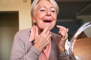 una donna anziana sorridente con una mano sul viso.